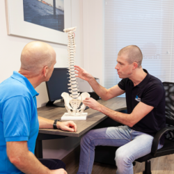 De manueel therapeut geeft manuele therapie in Papendrecht uitleg aan een man in een blauw shirt