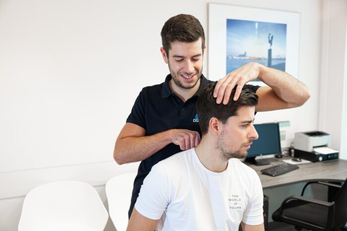 Man in een zwart shirt behandelt een patiënt in een wit shirt met fysiotherapie bij hoofdpijn en nekpijn