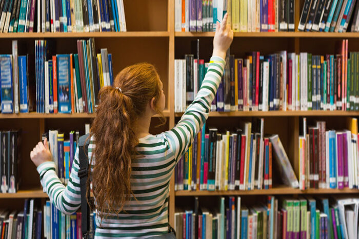 Frozen Shoulder Vrouw pakt een boek uit de kast en heeft last van een Frozen Shoulder