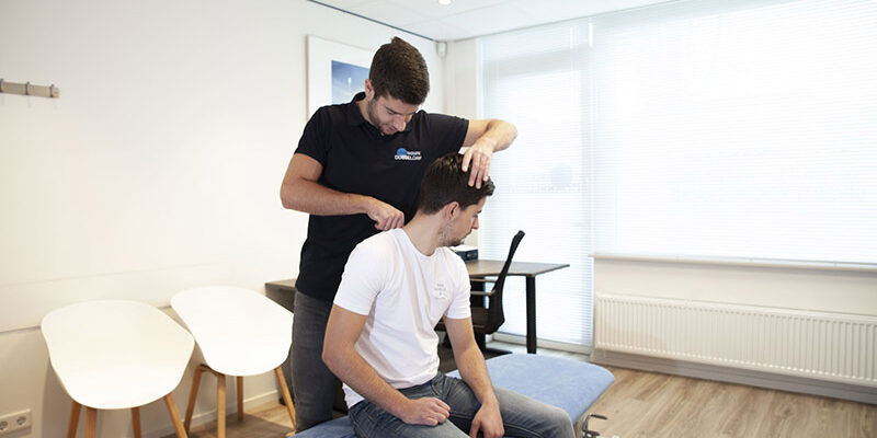 Manueel therapeut Reno Bosman in zijn Fysio Dubbeldam outft helpt patiënt Peter in het witte shirt zijn klachten door middel van manuele therapie in Sterrenburg