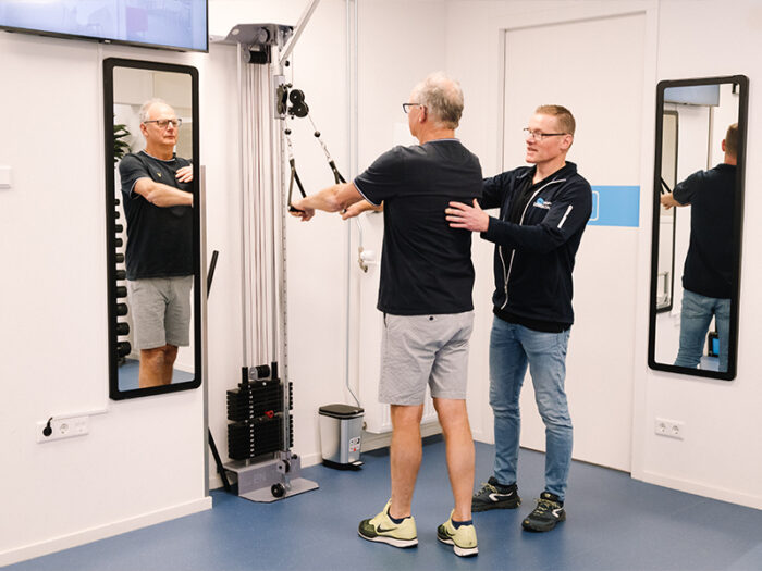 Schoudertherapie bij een slijmbeursontsteking Fysiotherapeut helpt patiënt met slijmbeursontsteking in de oefenzaal middels schoudertherapie