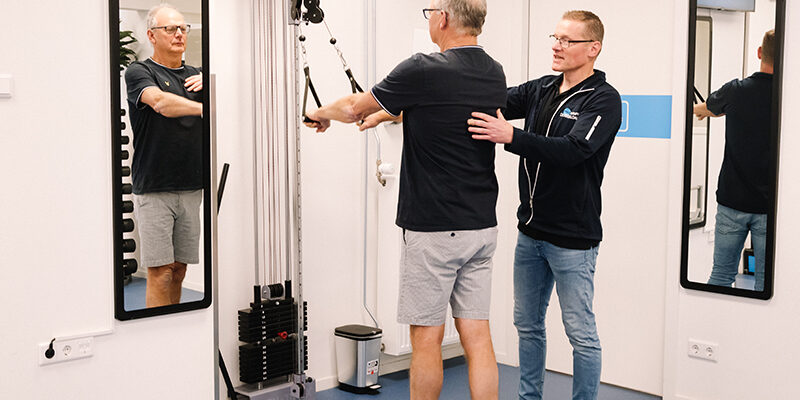Fysiotherapeut helpt patiënt met slijmbeursontsteking in de oefenzaal middels schoudertherapie