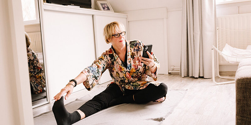 Vrouw zit in haar slaapkamer en voert mindfulness oefeningen uit die ze op haar telefoon krijgt van Fysiotherapie Dubbeldam