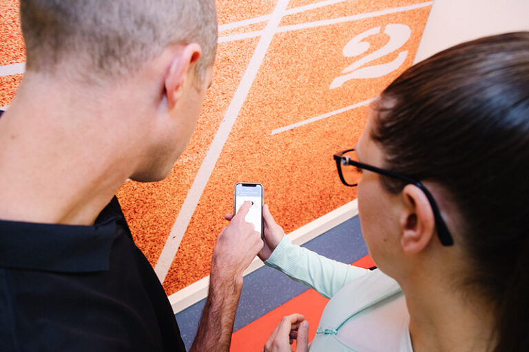 Een man en een vrouw staan in een hal. De vrouw heeft een mobiel vast, waarop een ervaring achtergelaten kan worden.