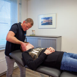 Fysiotherapeut in een zwart shirt behandelt een patiënt op de behandelbank met kaakfysiotherapie
