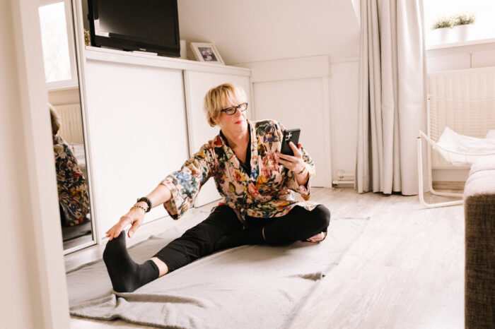 een vrouw met een telefoon in haar hand die dynamische rekoefeningen aan het doen is ten behoeve van een krachtige warming-up