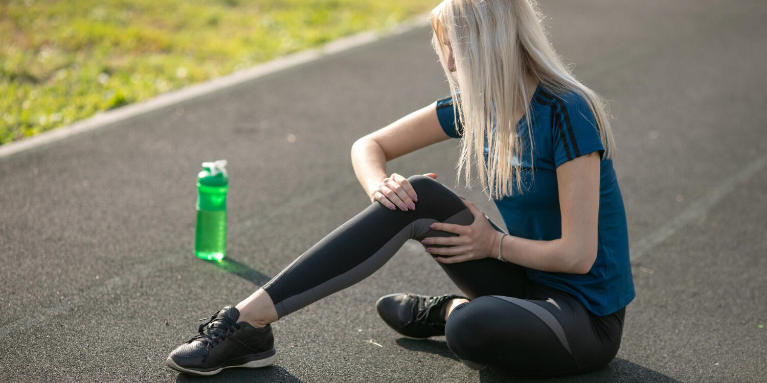 Vrouw in blauwe t-shirt. Houdt haar knie vast, want ze heeft last van een gescheurde meniscus.