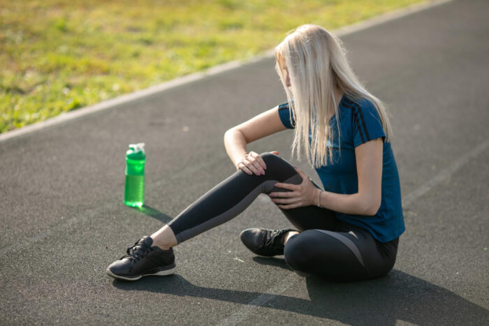 Vrouw in blauwe t-shirt. Houdt haar knie vast, want ze heeft last van een gescheurde meniscus.