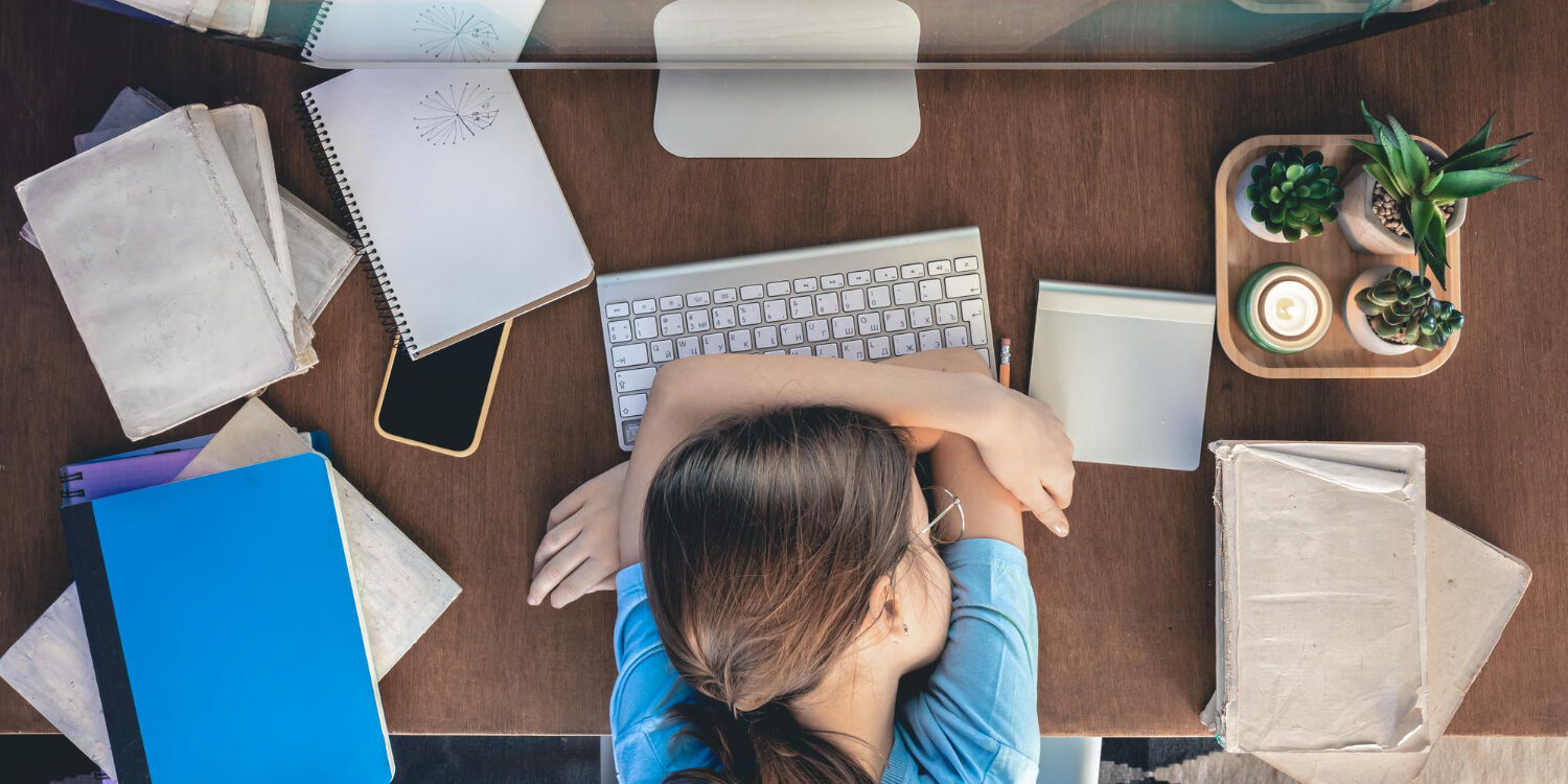 Vrouw ligt vermoeid over haar bureau, omdat ze last heeft van klachten bij een burn-out.