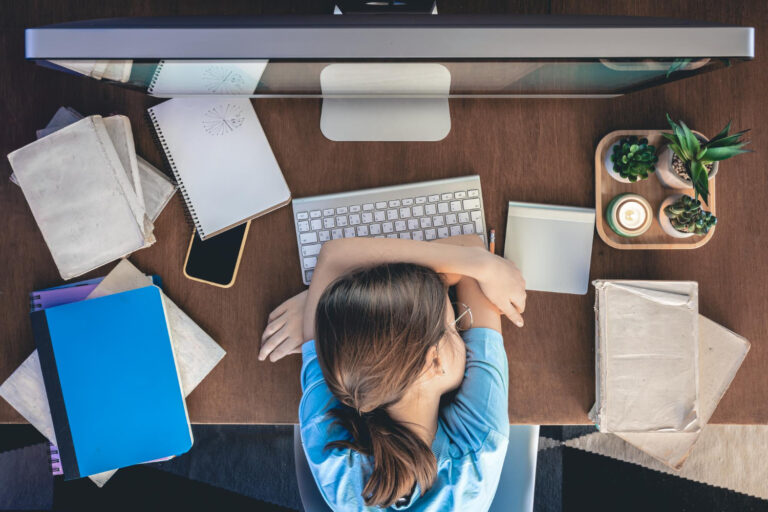 Vrouw ligt vermoeid over haar bureau, omdat ze last heeft van klachten bij een burn-out.