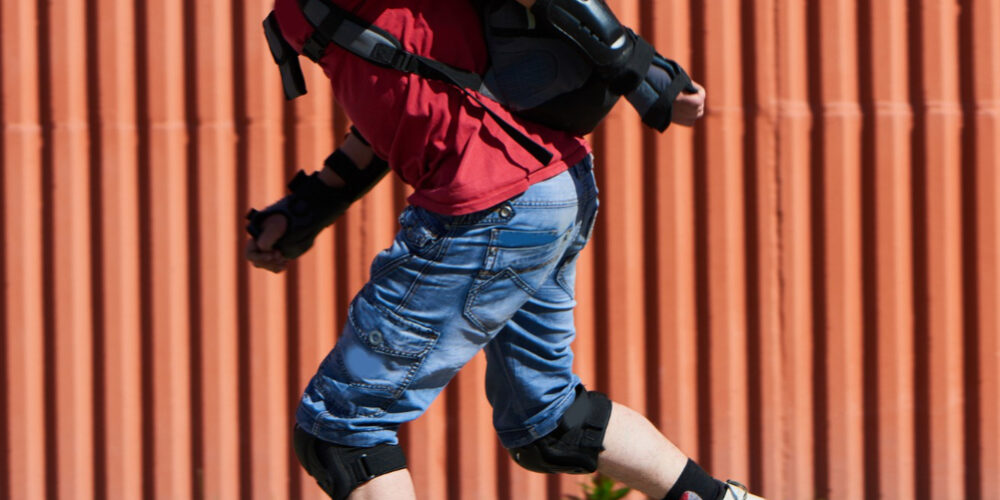 Man in rood t-shirt is aan het skeeleren met heel veel bescherming aan. Dit doet hij, omdat hij veel last had van blessures door het skeeleren.