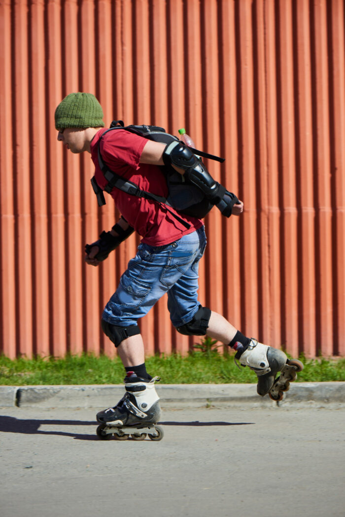 Man in rood t-shirt is aan het skeeleren met heel veel bescherming aan. Dit doet hij, omdat hij veel last had van blessures door het skeeleren.