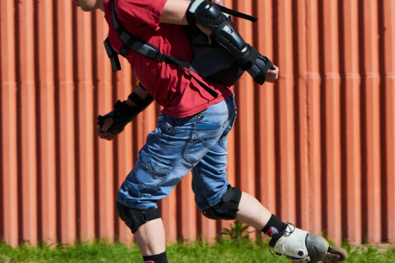Man in rood t-shirt is aan het skeeleren met heel veel bescherming aan. Dit doet hij, omdat hij veel last had van blessures door het skeeleren.